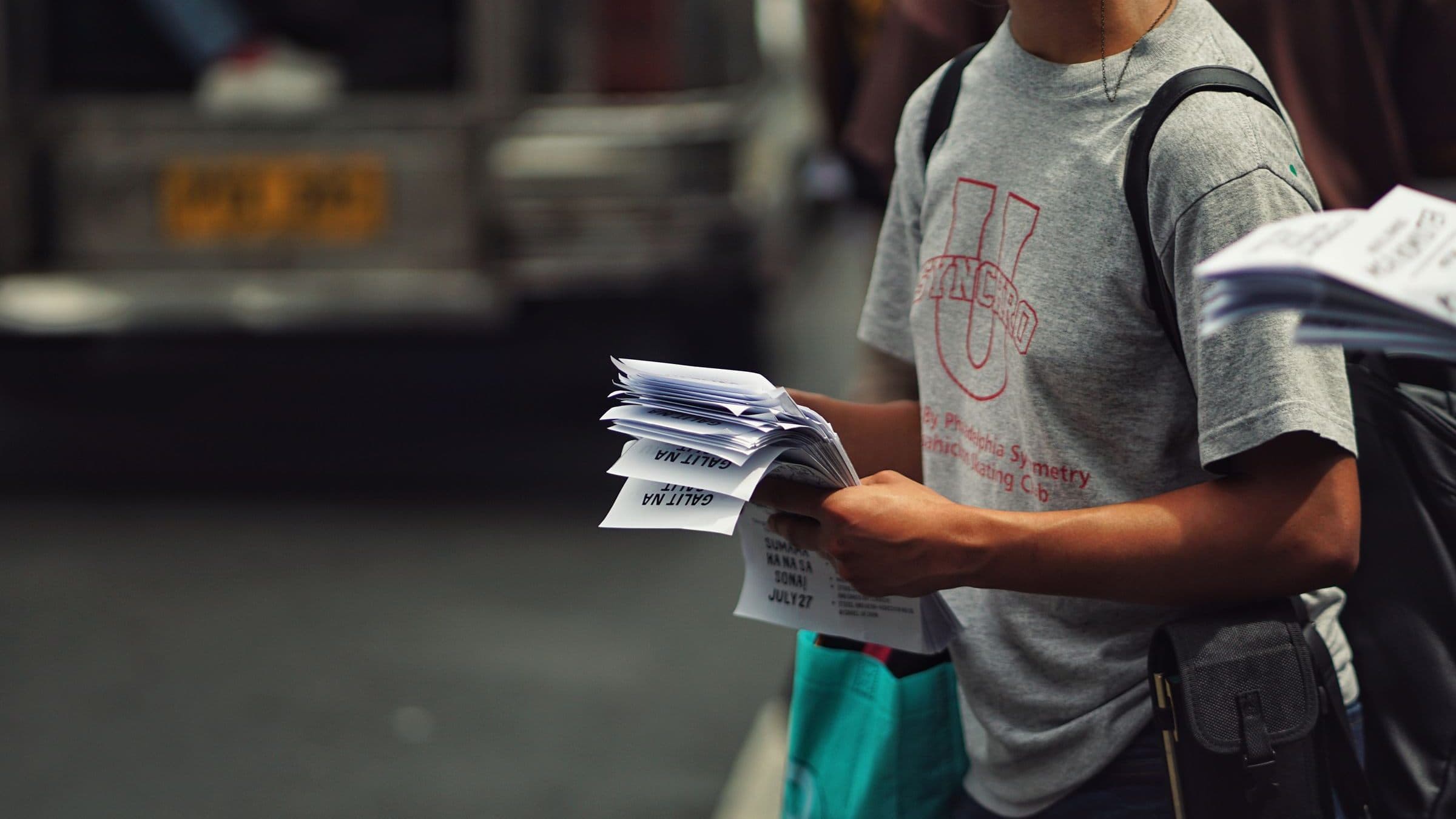 A person holding a stack of printed flyers on a street.
