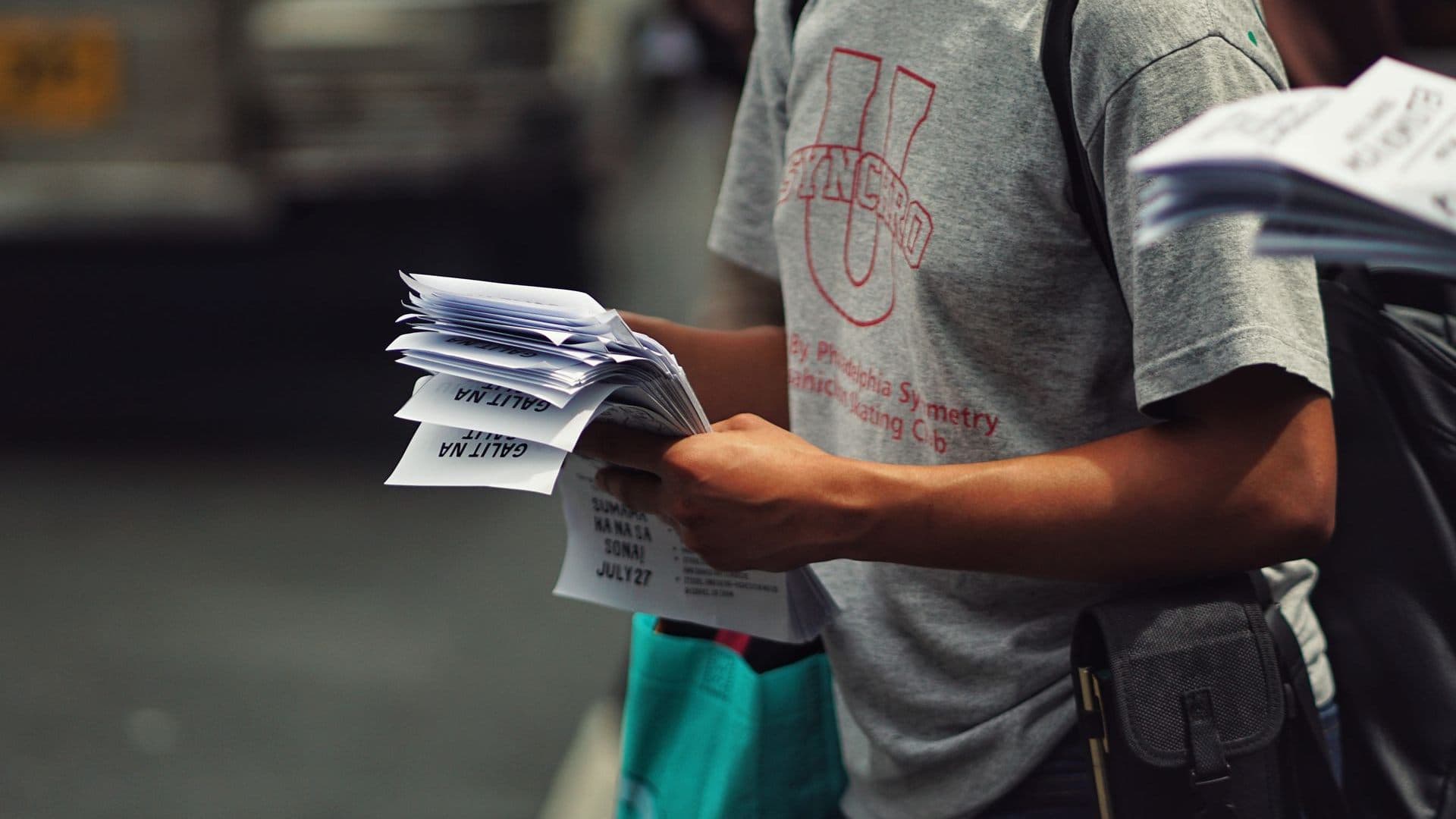 A person holding a stack of printed flyers on a street.