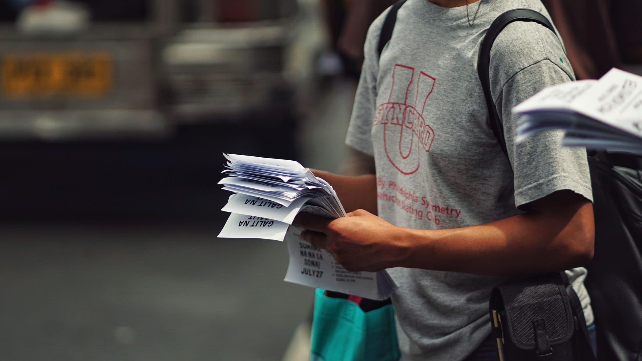 A person holding a stack of printed flyers on a street.